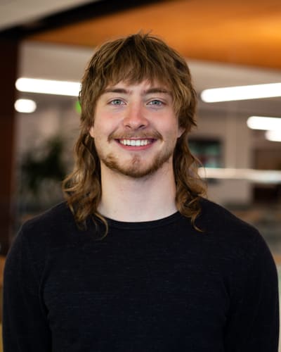Portrait of Calvin Hickey smiling, wearing a dark sweater in a warmly lit room